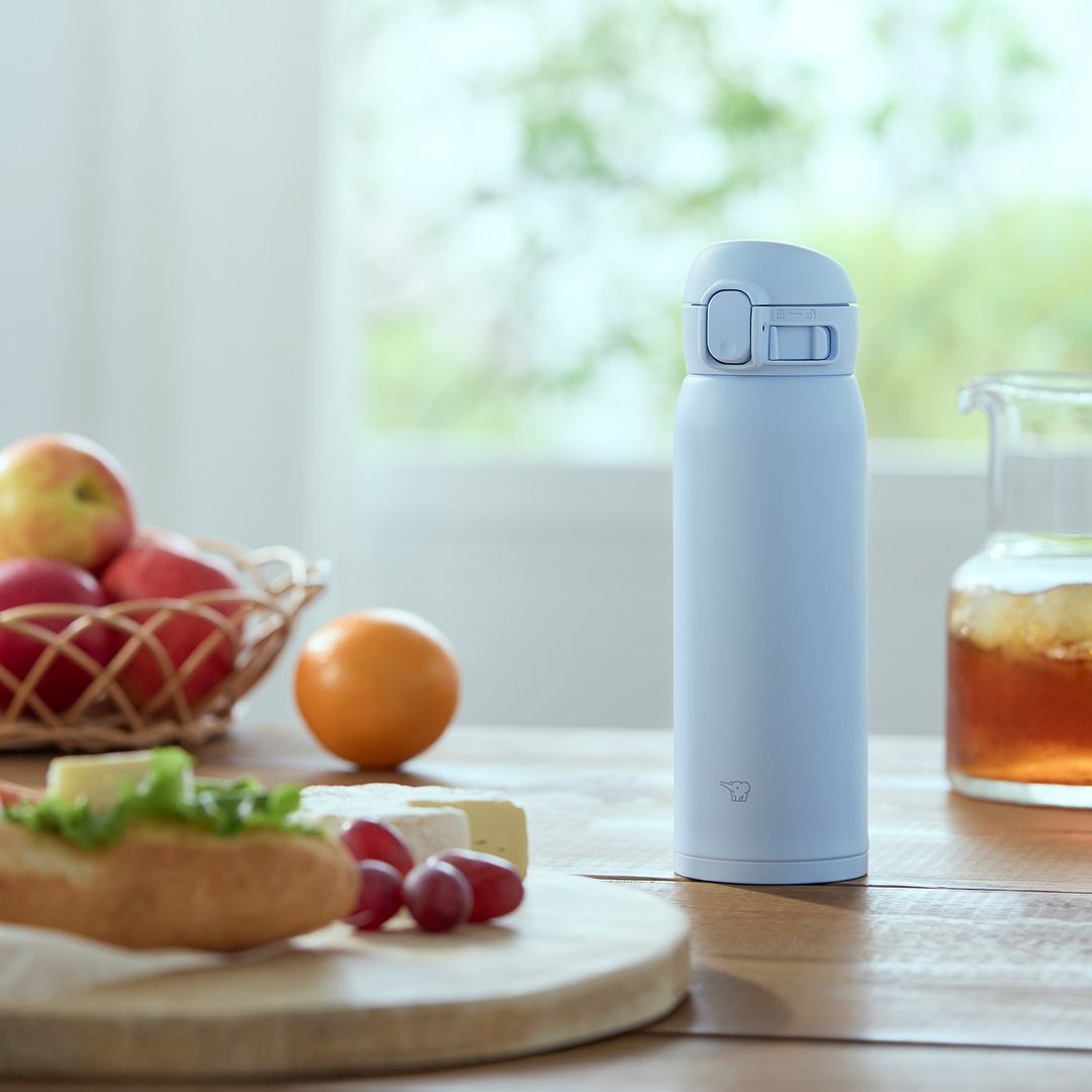 White insulated travel mug on kitchen table with fruit and juice – ideal for hot or cold drinks in Kuwait